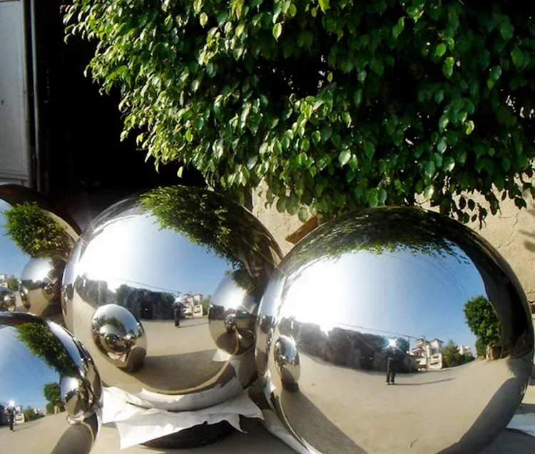 Polished stainless steel mirror-finish hollow spheres displayed outdoors beneath green foliage