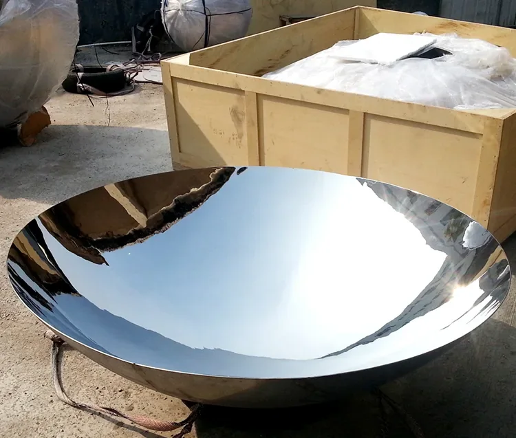 Large polished stainless steel hemispherical dish on a concrete floor beside a wooden
