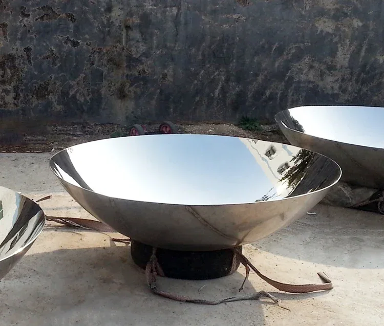 Large polished stainless steel hemispherical bowls resting on a concrete floor outdoors