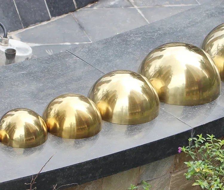Row of polished golden metal hemispheres in ascending sizes on a dark stone ledge outdoors