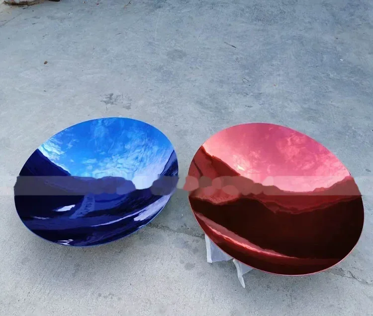 Two polished concave metal dishes, one reflecting blue and one red, lying on a concrete floor