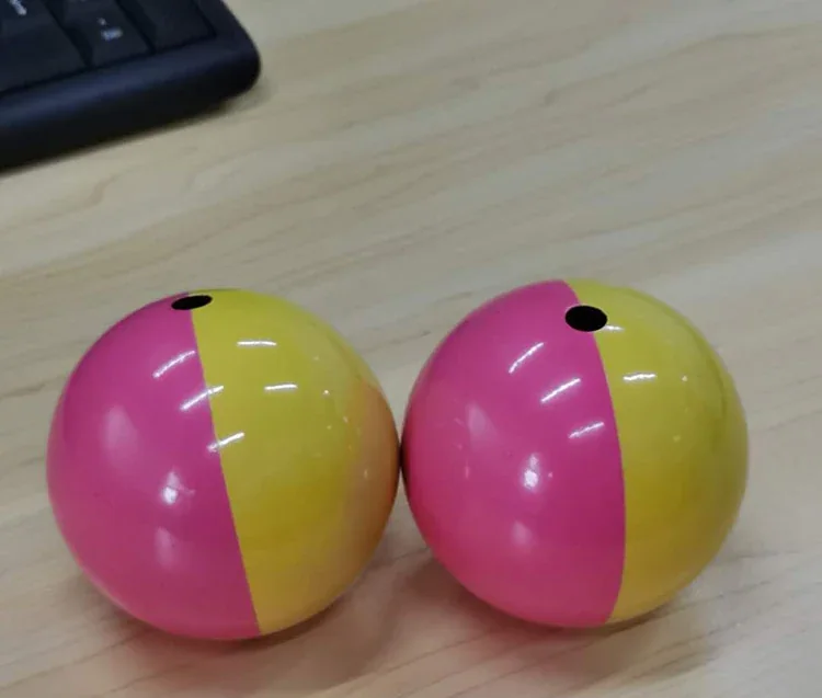 Two pink and yellow two-tone balls with small holes on top resting on a wooden desk next to a keyboard