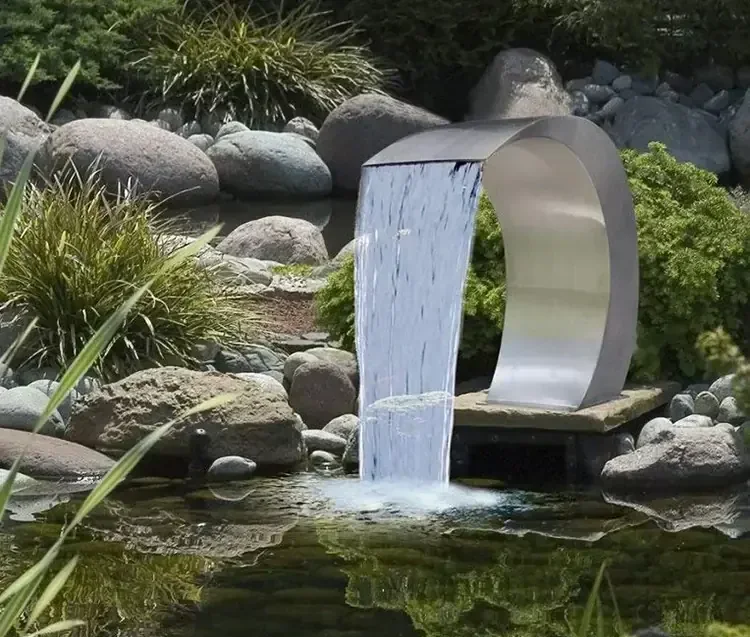 Curved stainless steel waterfall fountain spout pouring into a landscaped garden pond