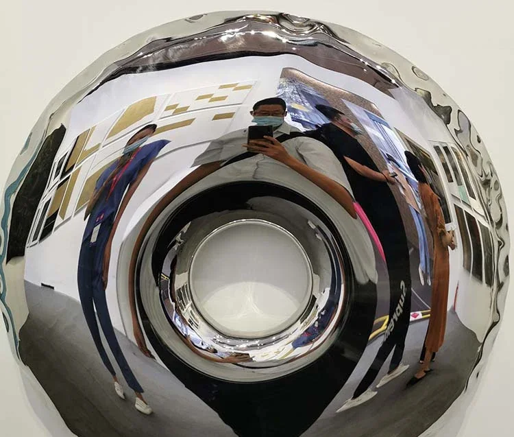 Close up of a polished chrome wheel cap reflecting the photographer and surrounding environment.