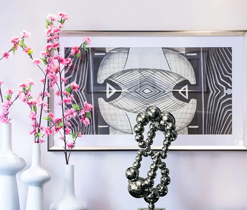 Decorative home interior featuring white vases with pink flowers, a metal sphere sculpture, and framed abstract art.