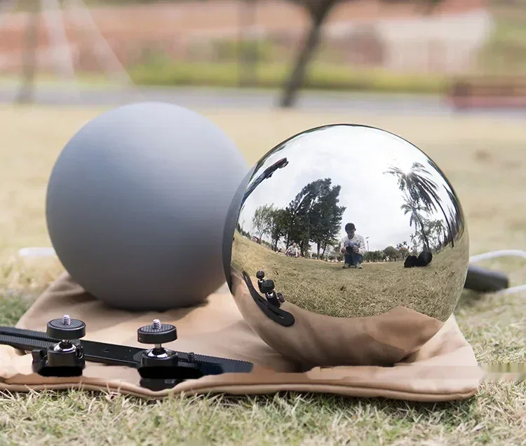 A matte gray sphere and a reflective chrome sphere with a mounting bracket resting on a cloth outdoors