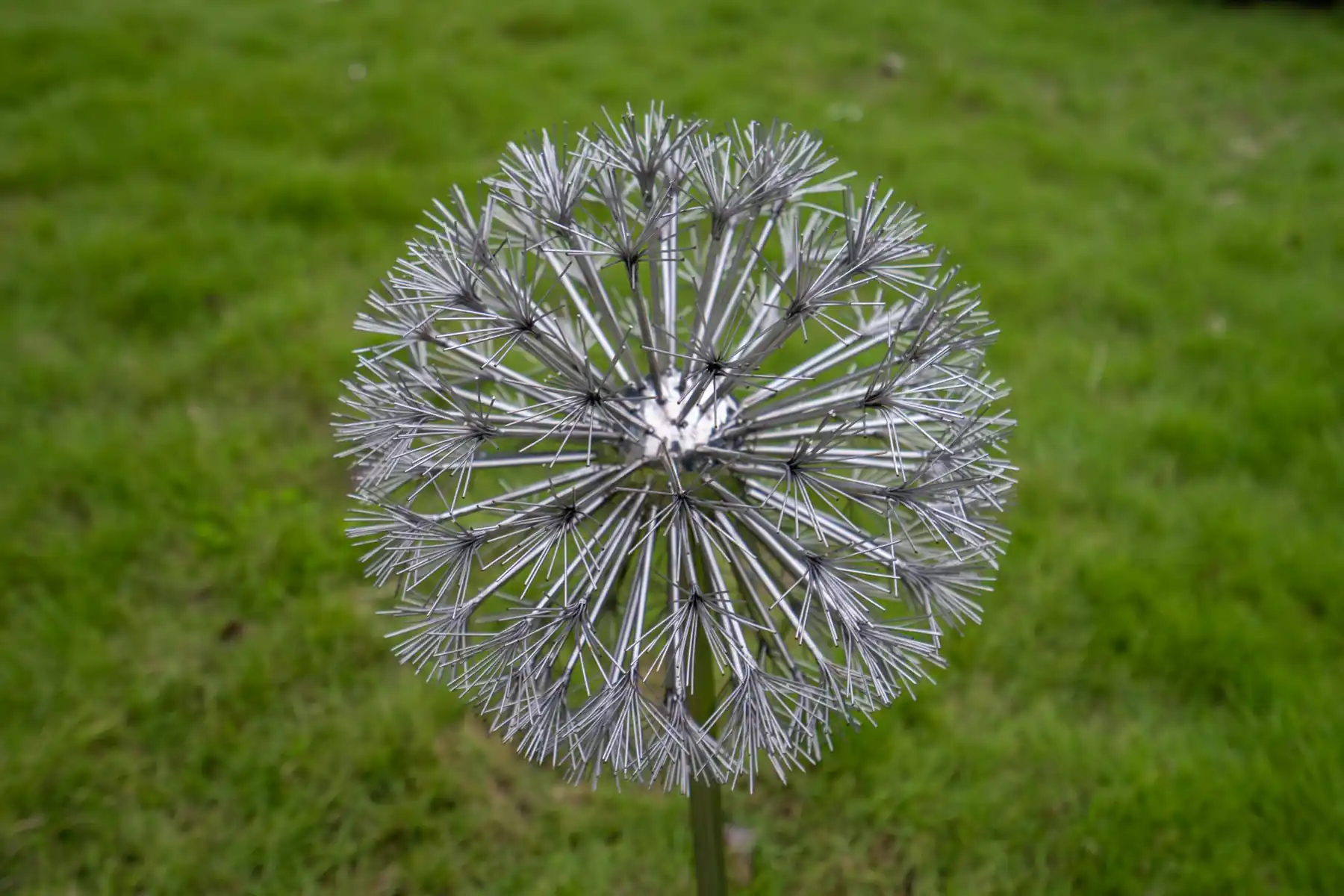 Stainless steel sphere sculpture with radiating rods standing on a lawn