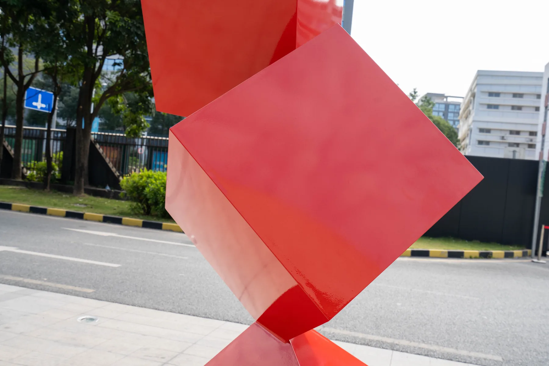 Large red geometric cube sculpture installed on a city sidewalk