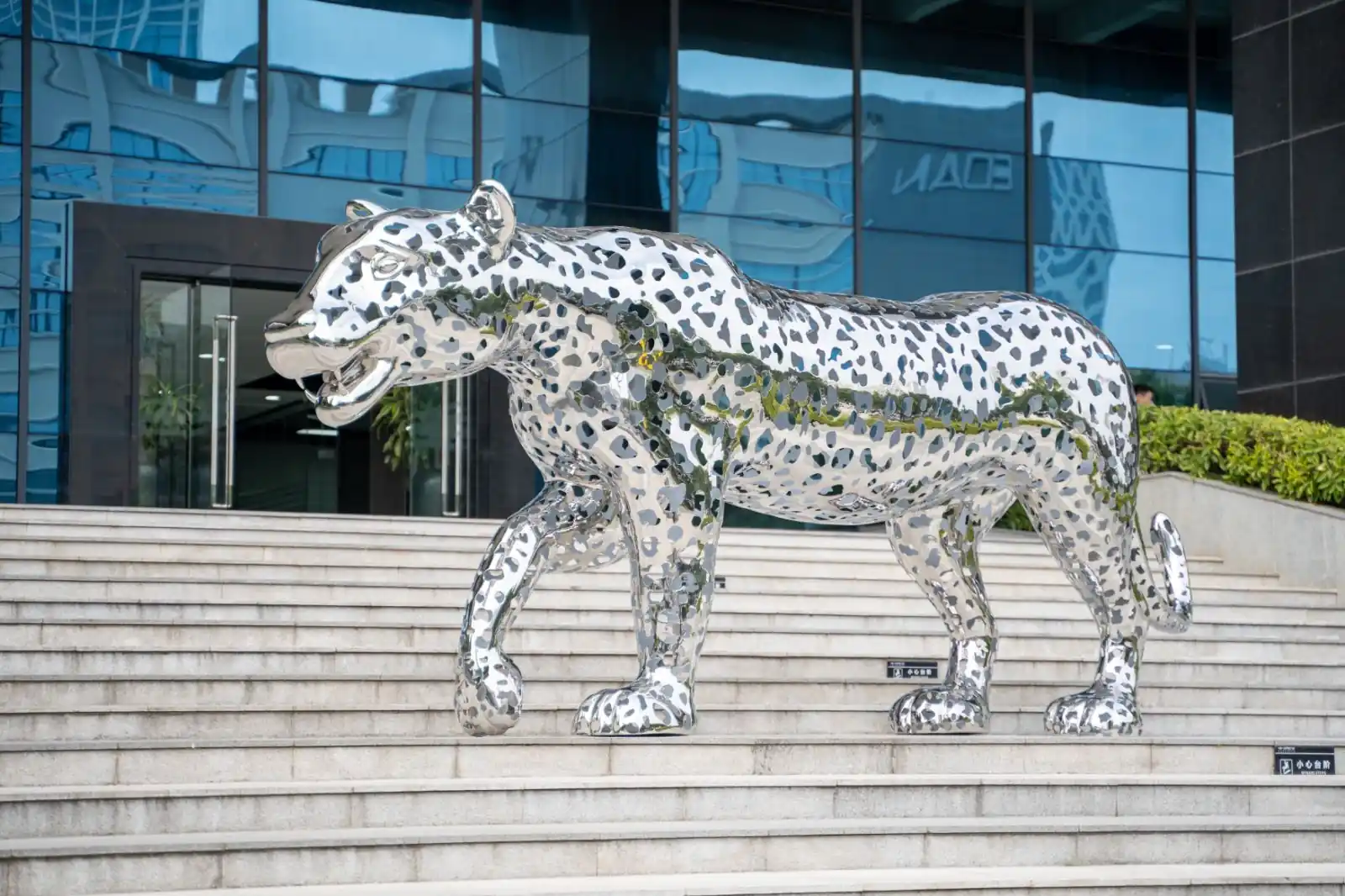 Hollow leopard sculpture in patterned stainless steel on public stone steps