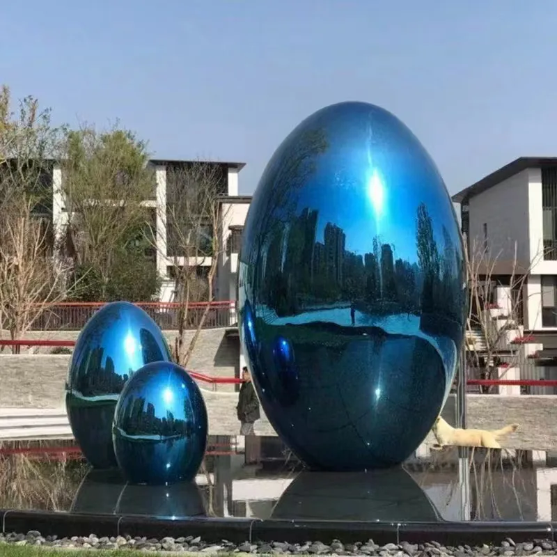 Three mirror polished blue egg shaped stainless steel sculptures in a courtyard
