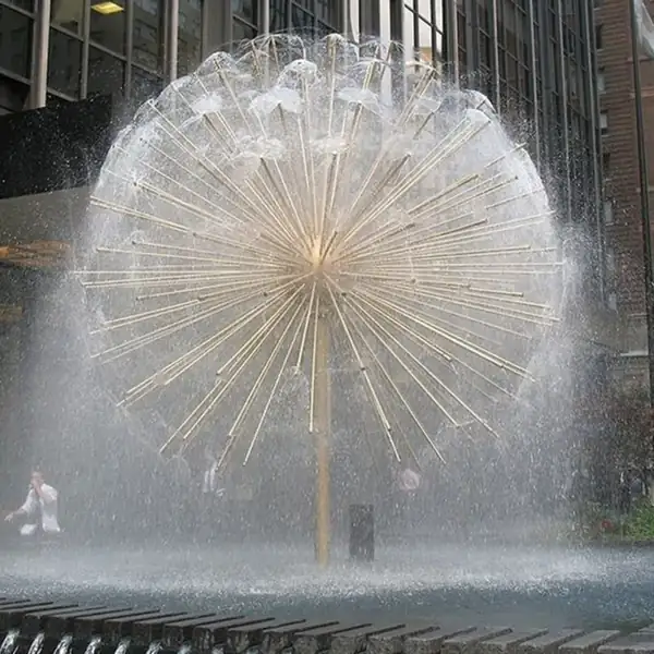 Spherical dandelion-style fountain with radiating golden pipes spraying water in a city plaza surrounded by tall buildings