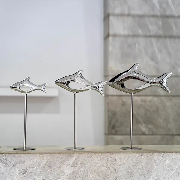 Three chrome fish sculptures on slim metal stands of increasing height, displayed on a white marble ledge