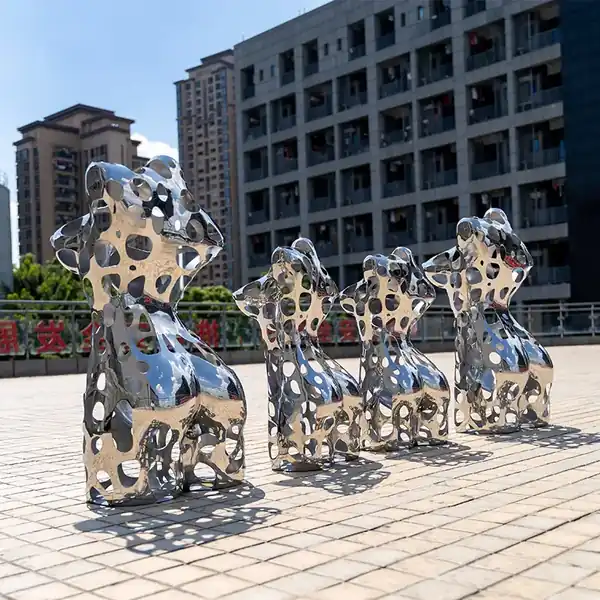 Four shiny perforated metal sculptures of animals standing on a paved plaza in front of apartment buildings.