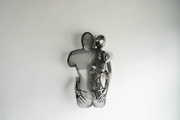 Chrome and wire mesh sculpture of two embracing figures on a wall
