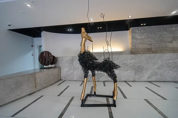Deer sculpture with gold legs and textured body displayed on a plinth