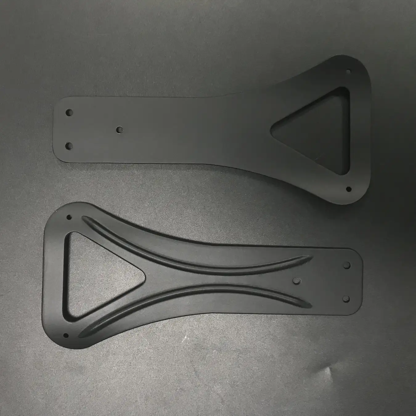 Machined carbon fiber structural arms with matte finish laid on a workbench