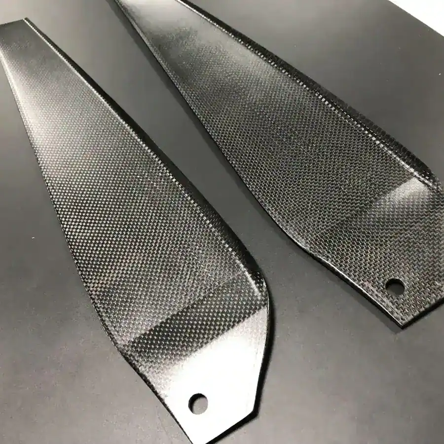 Carbon fiber blade prototype with a woven surface on a grey workbench