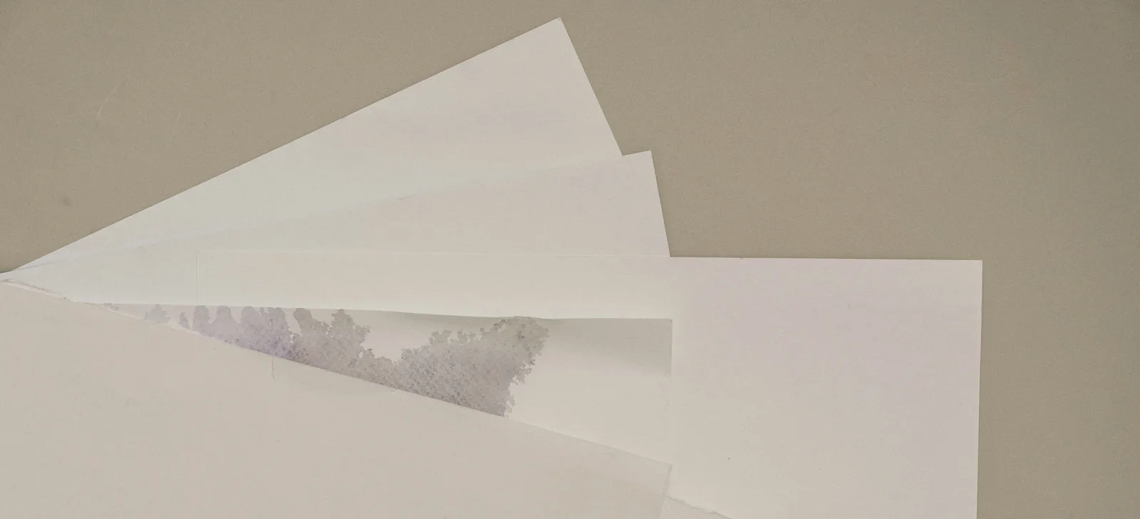 Sheets of white uncoated paper fanned out on a neutral grey surface