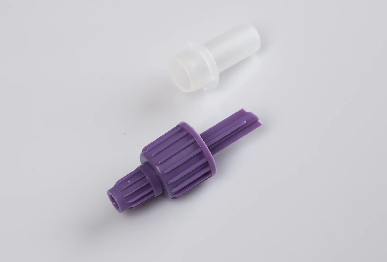 Purple plastic connector fitting shown next to a translucent white cap on a neutral background.