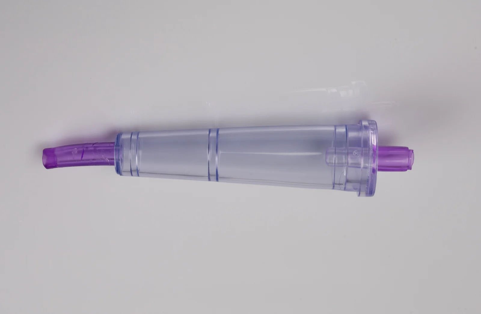Clear plastic cylindrical component with purple ends on a white surface.