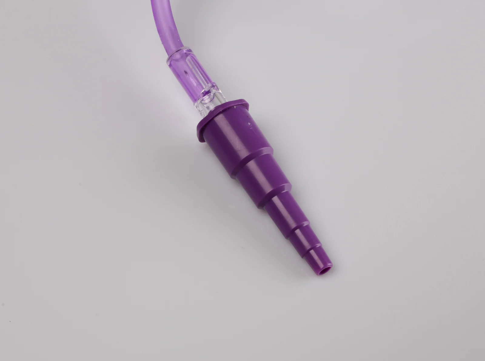 Purple stepped medical connector with tubing on plain background