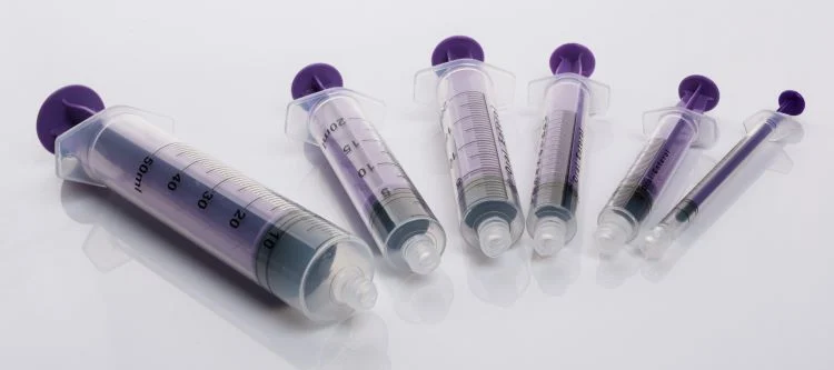 Various sizes of plastic medical syringes with purple plungers on a white reflective surface