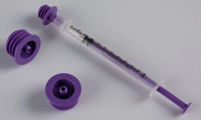 Enteral syringe with purple plunger and bottle adapters on neutral background