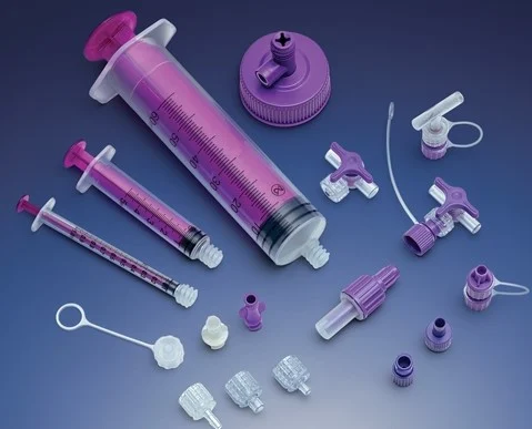 Purple enteral syringes, connectors, valves, and caps arranged on a blue gradient surface