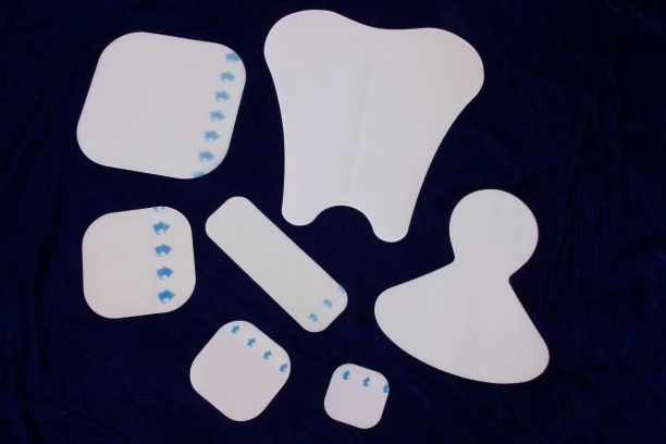 Assorted white medical adhesive dressings in various shapes laid on dark fabric