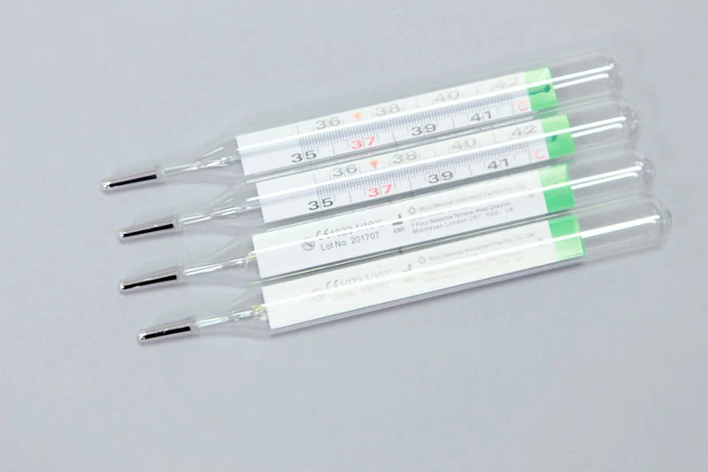 Four glass clinical thermometers displayed on a plain light gray background