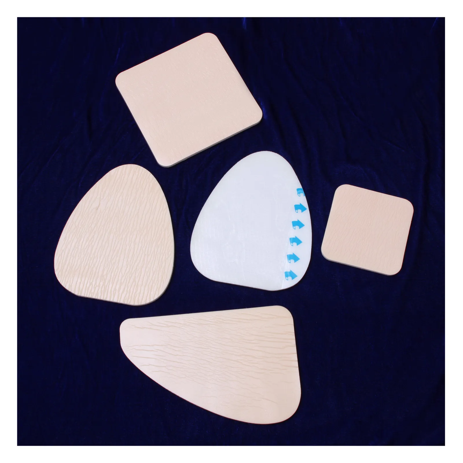 Assorted skin-tone adhesive patches and pads in various shapes on dark blue fabric