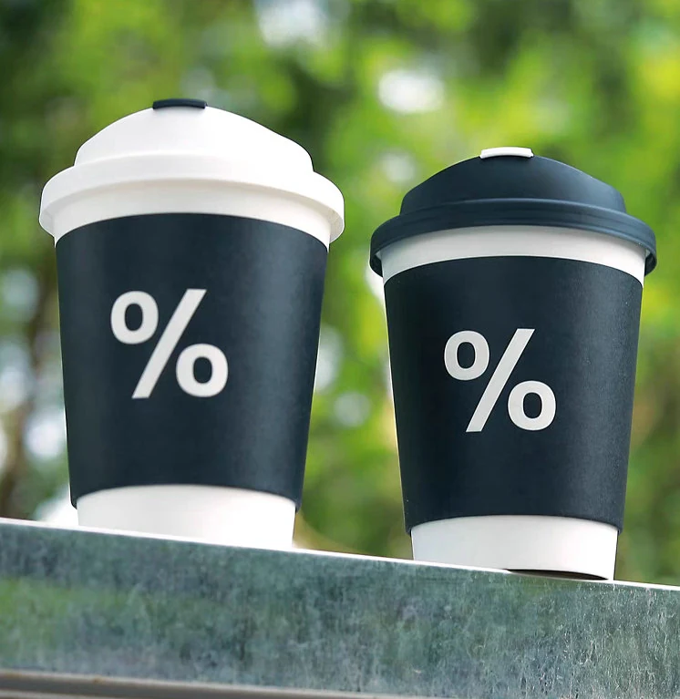 Printed disposable coffee cup held to show the insulated outer wall