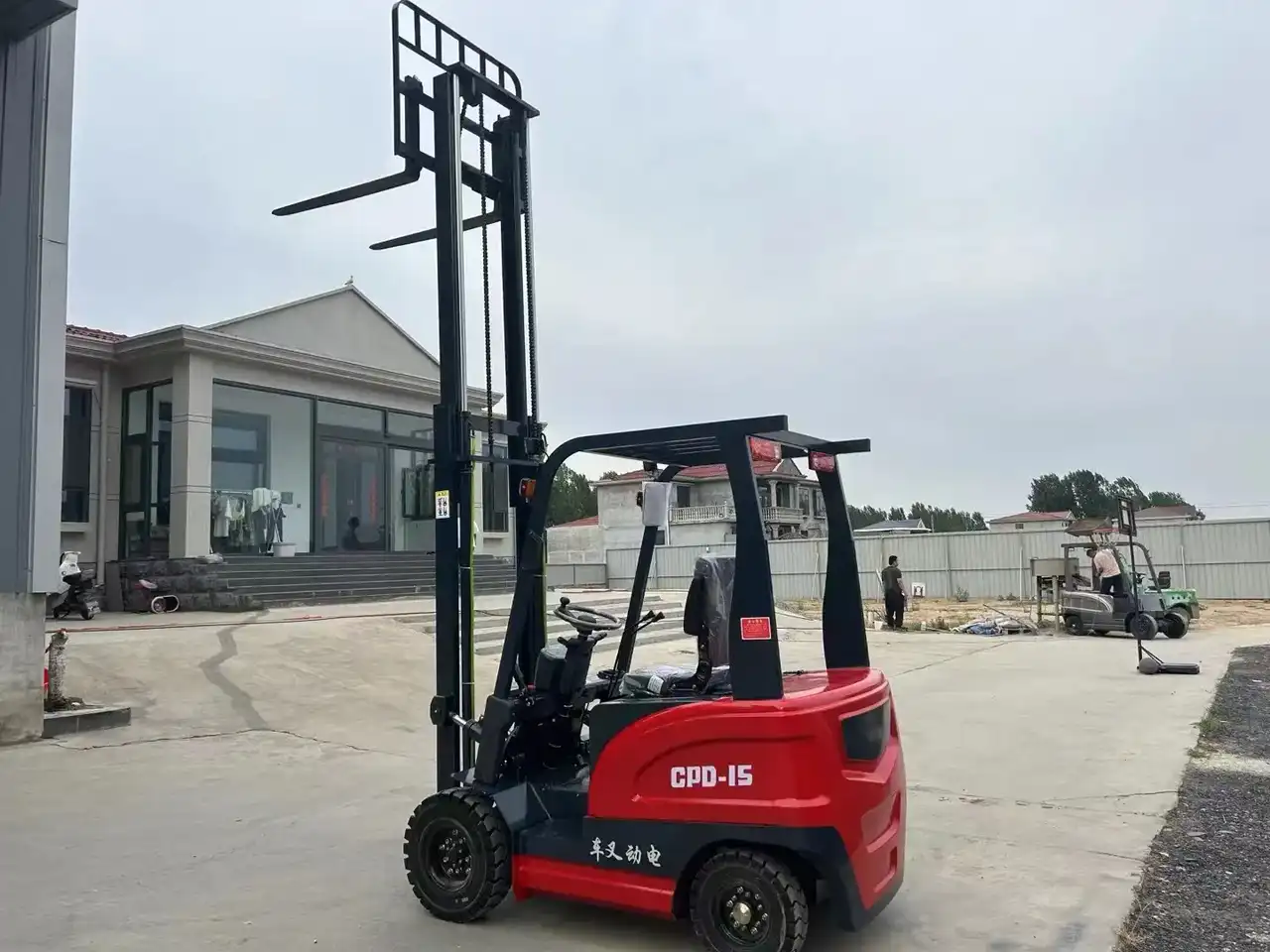 Red 4x4 electric forklift on a gravel yard, front view with forks raised