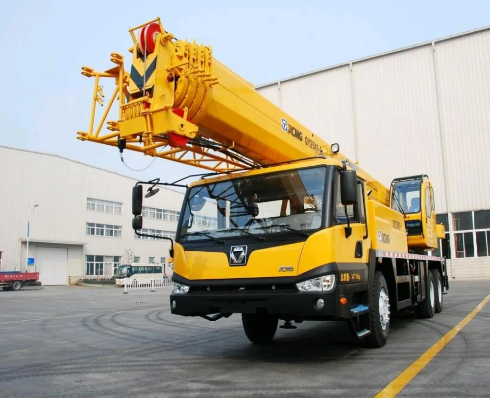 Yellow mobile crane with extended boom parked outside a factory building.