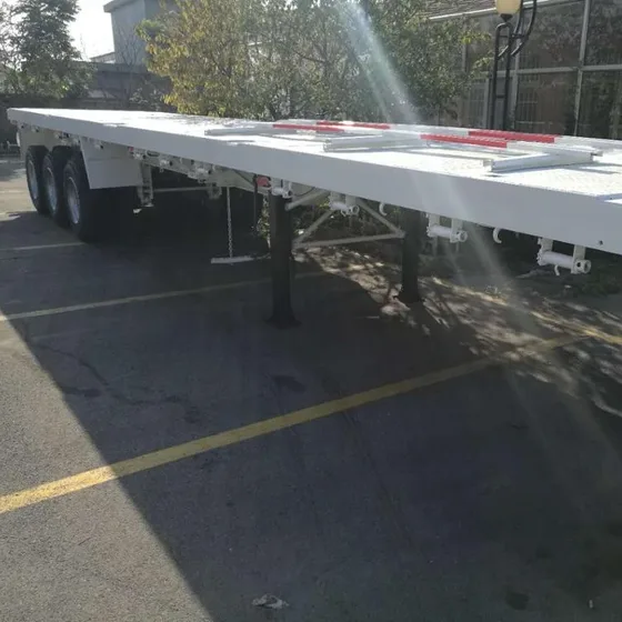 3-axle flatbed trailer parked on a yard, front three-quarter view showing 13000mm length and 1200R20 tyres