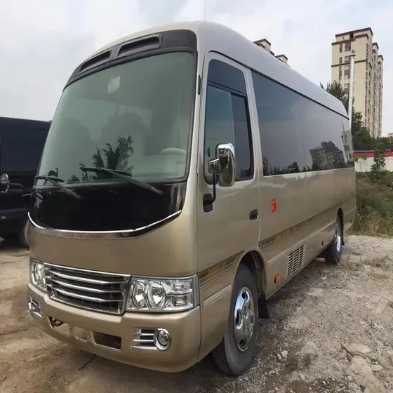 Used Toyota Coaster mini bus parked on a yard, front three-quarter view with visible side logo