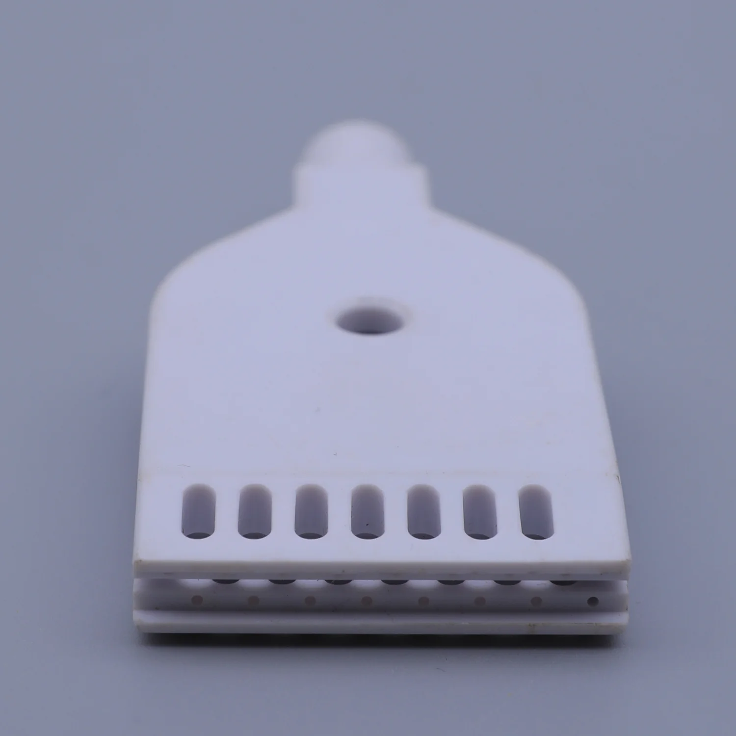 White plastic component with a mounting hole and a row of eight vertical slots on a gray background