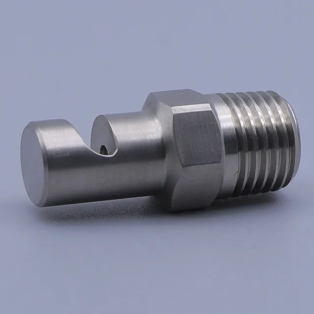 A stainless steel threaded fitting with a notched end and a small orifice, resting on a gray surface