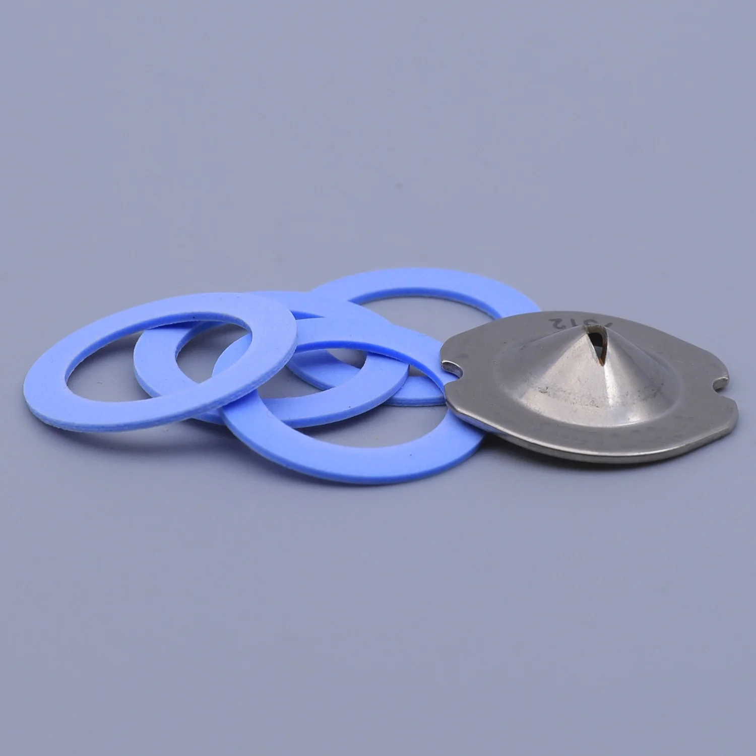 A stainless steel rupture disc and four blue silicone gaskets arranged on a grey background
