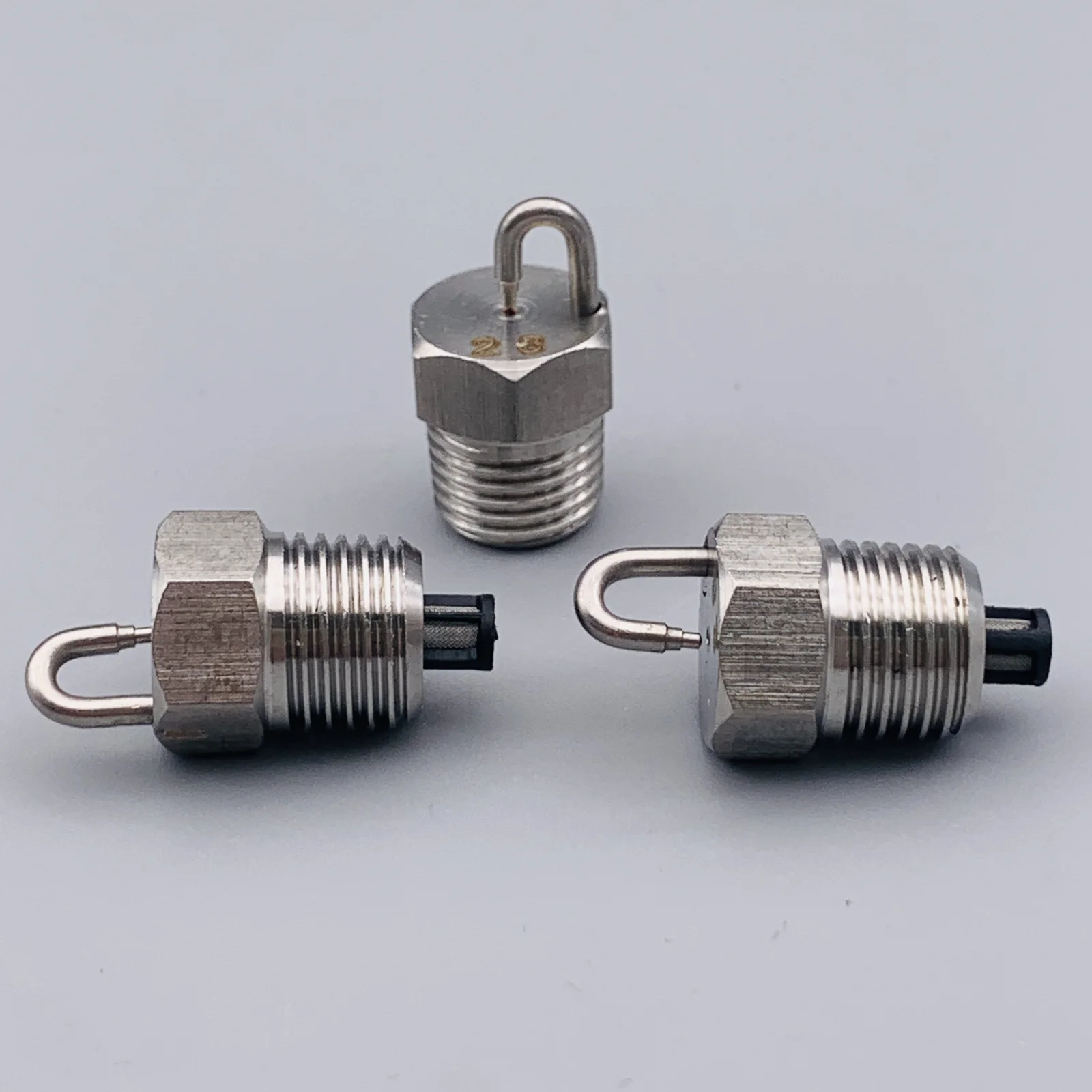Three metallic threaded connectors with hex bodies, eye loops, and black plastic ends on a gray background