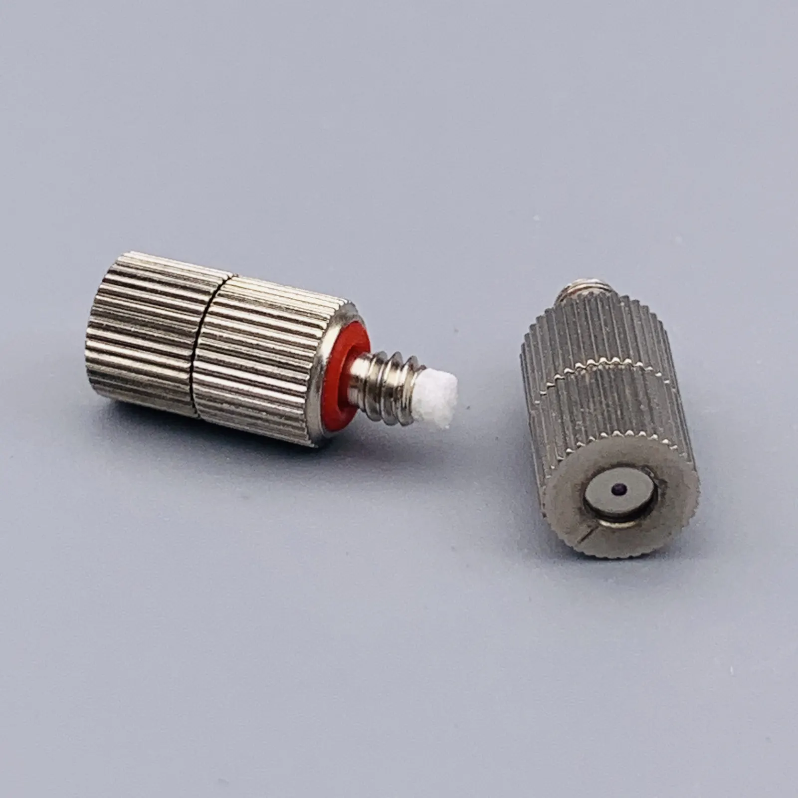 Two knurled metal pneumatic fittings with red seals on a gray background