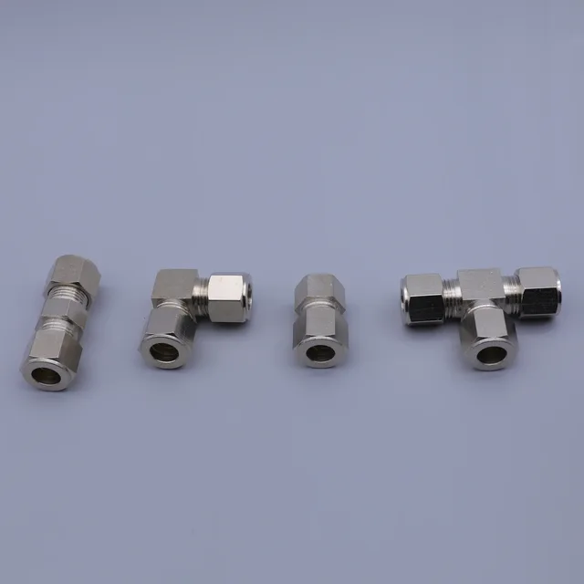 A collection of four stainless steel tube fittings including straight, elbow, and tee connectors on a gray background