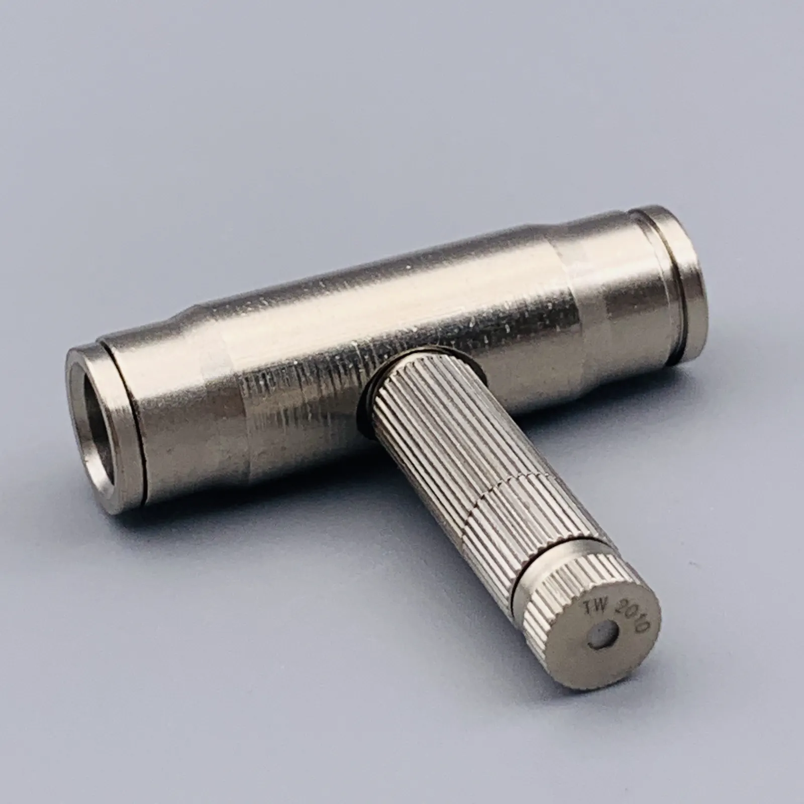 Silver metal T-shaped connector with knurled grip on a gray background
