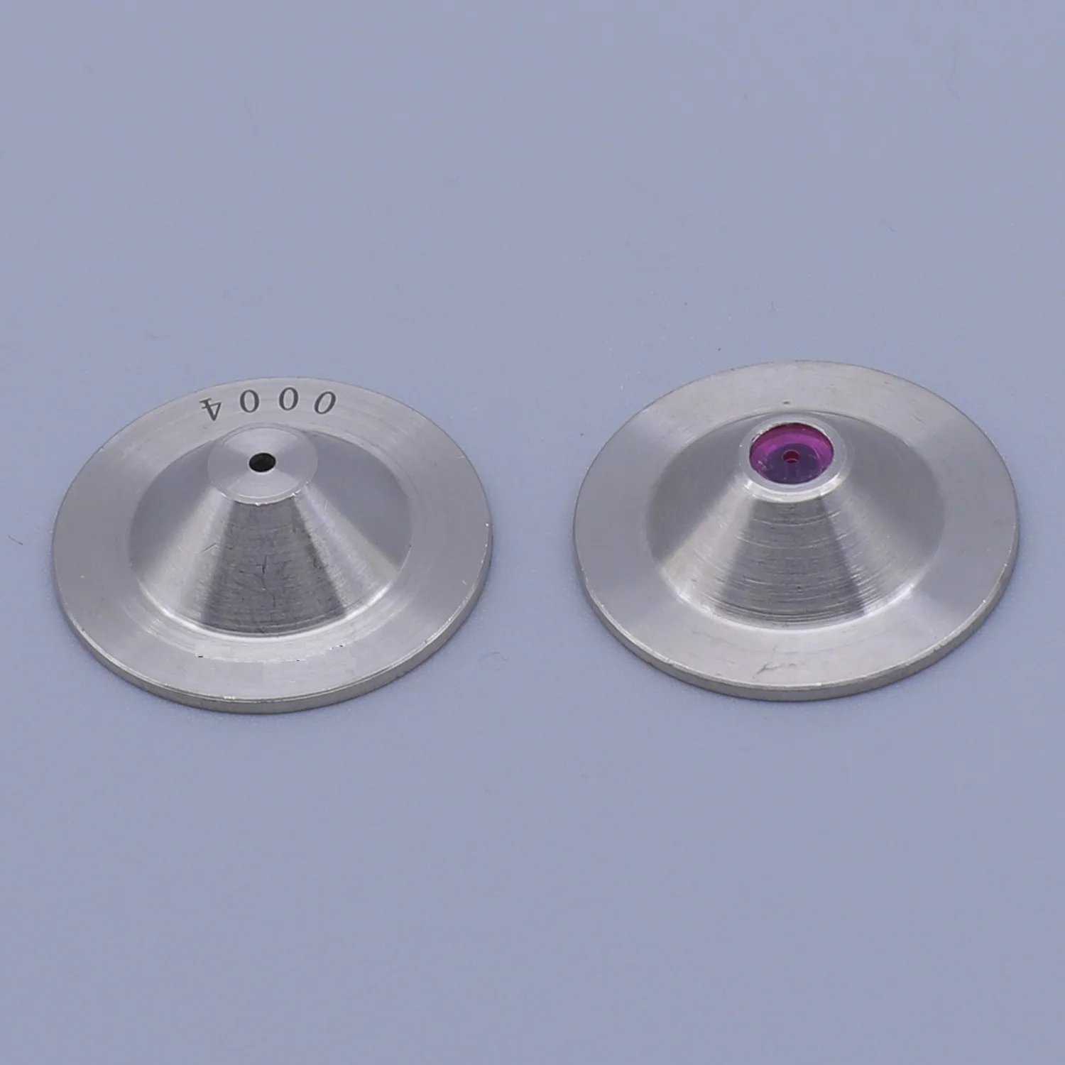 Two silver conical metal discs with central holes, one featuring a purple gem insert
