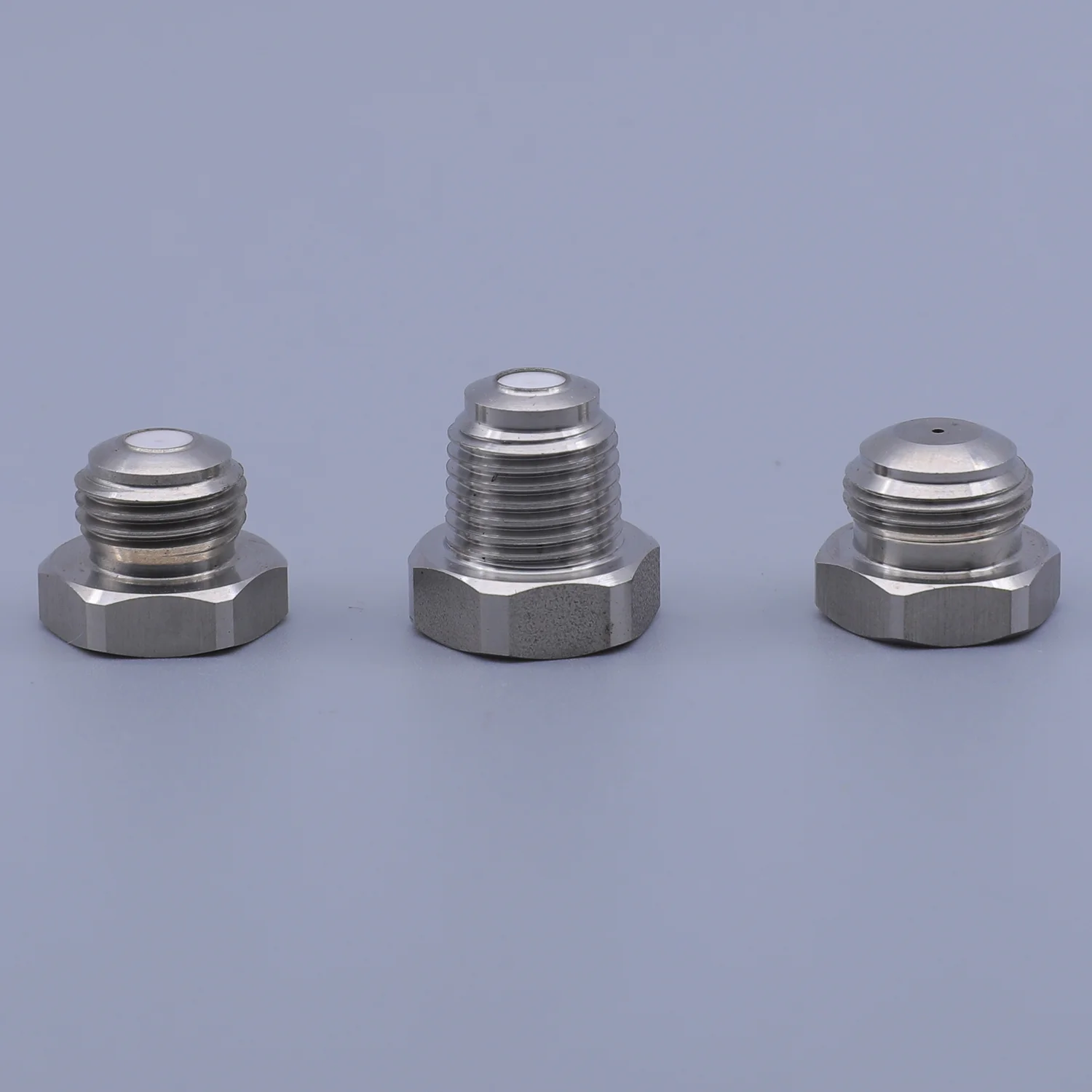 Three stainless steel hexagonal threaded caps arranged in a row against a solid blue background