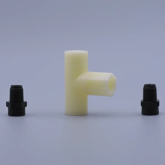 A cream colored T-shaped plastic component flanked by two black threaded fittings