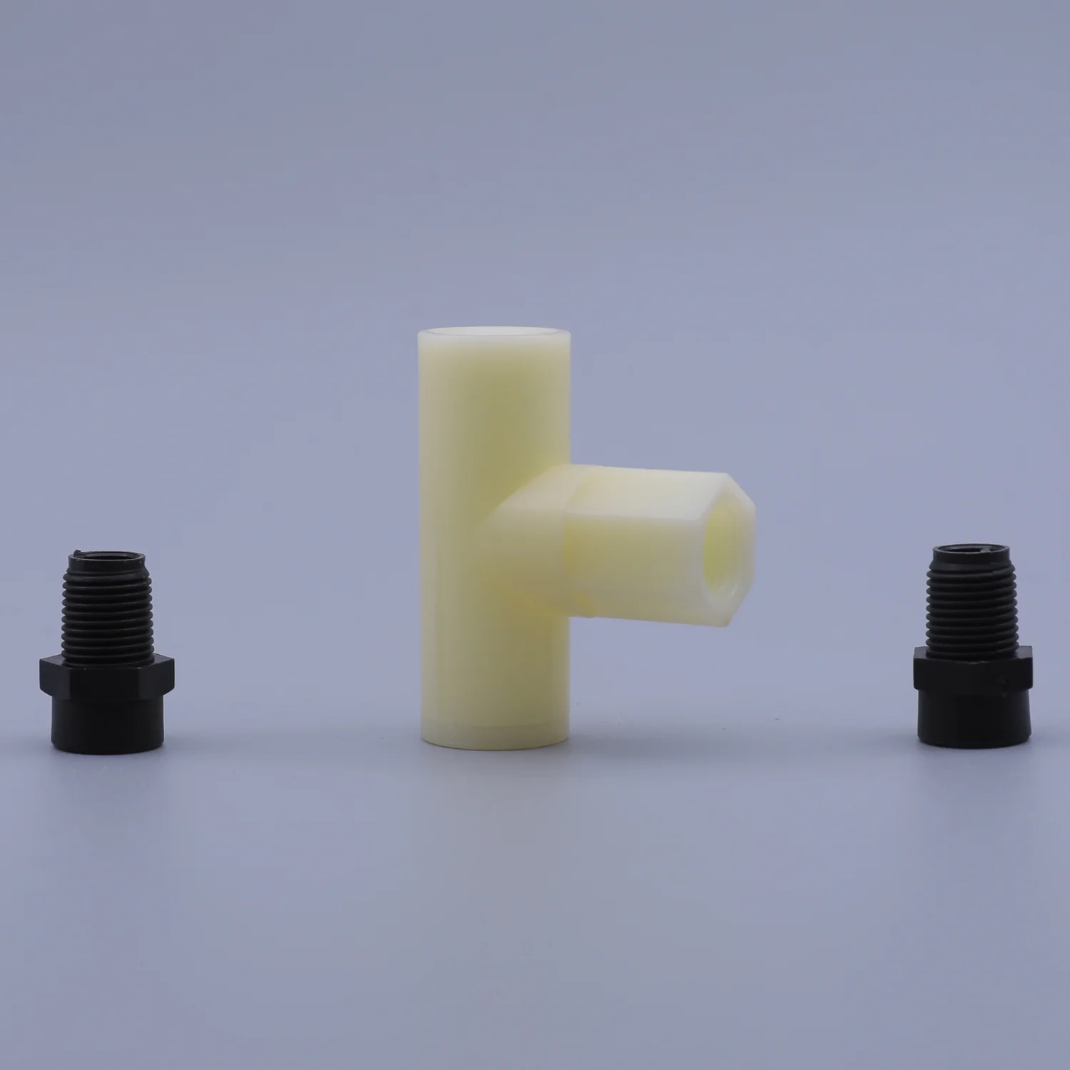 A cream colored T-shaped plastic component flanked by two black threaded fittings
