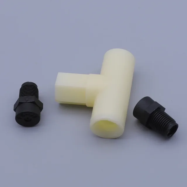 A white plastic T-shaped connector lying between two black threaded fittings on a gray background