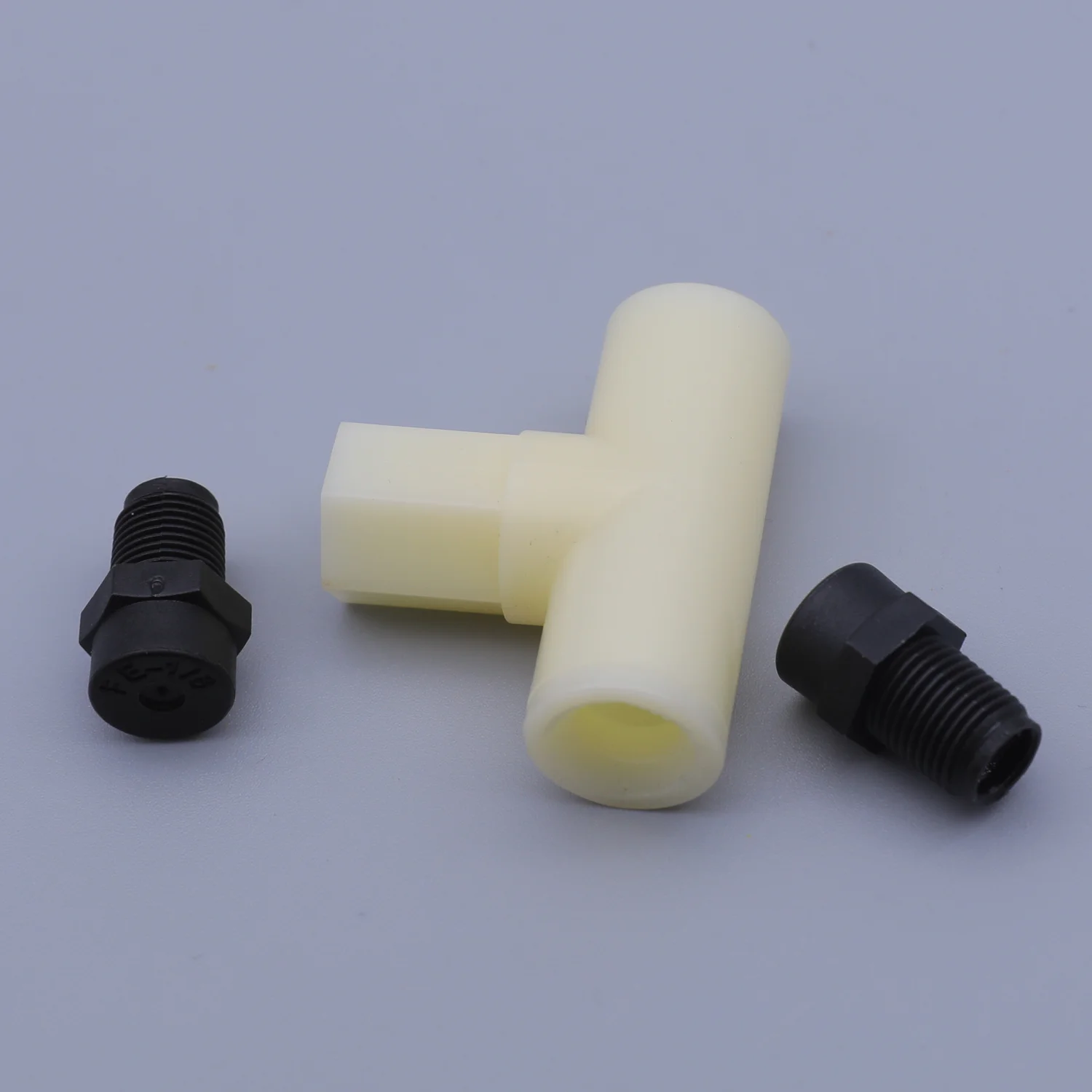 A white plastic T-shaped connector lying between two black threaded fittings on a gray background