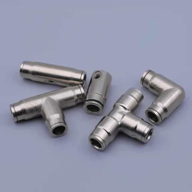 Several silver metal pneumatic push-to-connect fittings, including elbows and tees, arranged on a plain background